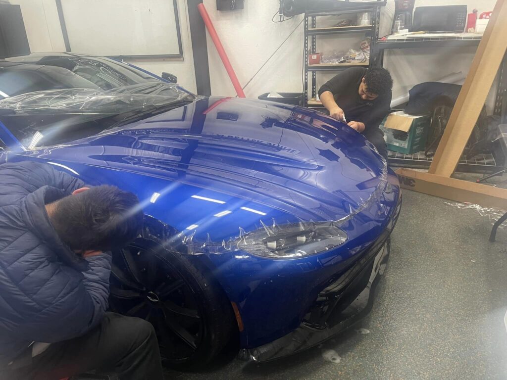 workers putting paint protection on aston martin